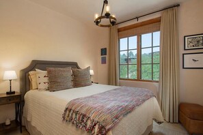 Una camera da letto con un letto grande, un comodino con una lampada, una finestra con tende e un quadro appeso al muro.