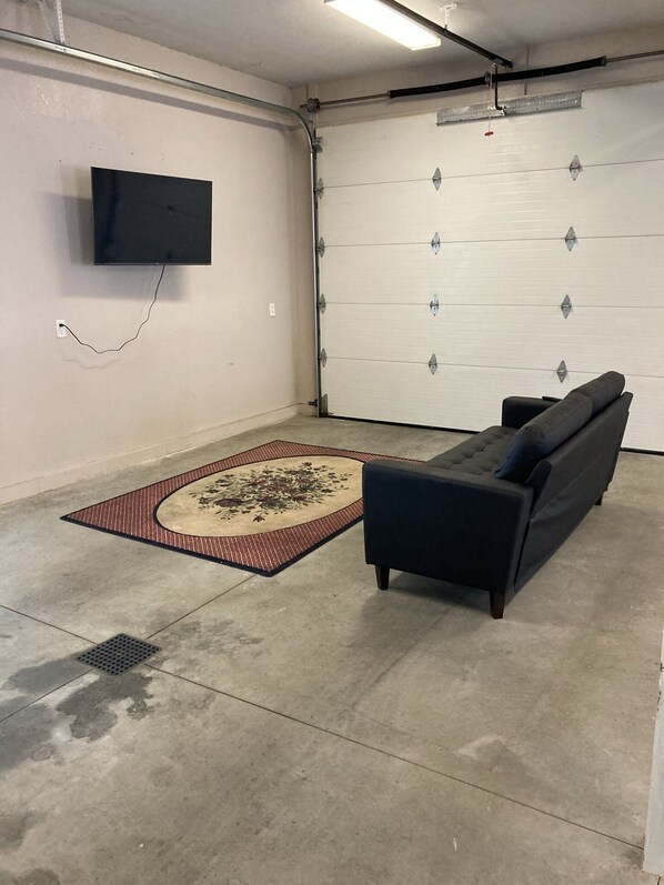En garage med et fladskærms-tv ophængt på væggen, en mørk sofa og et mønstret tæppe på gulvet.