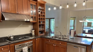 Una cocina con armarios de madera, electrodomésticos de acero inoxidable, una vinoteca integrada e iluminación colgante.