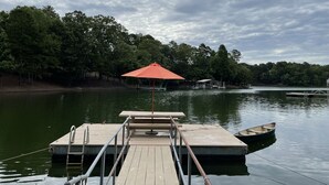 Muelles de madera que se adentran en un lago, con una sombrilla roja, rodeados de árboles frondosos.