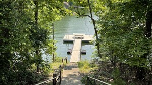 Una escalera de madera que conduce a un muelle sobre un lago tranquilo, rodeado de abundante follaje verde.