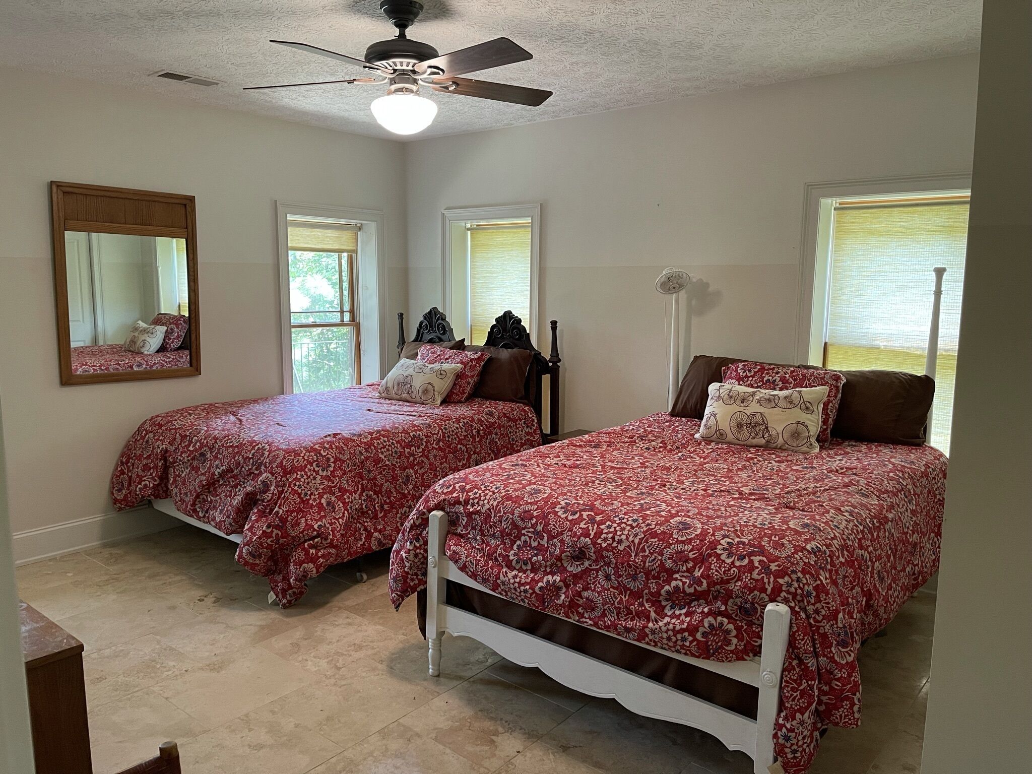 A bedroom with two beds, a ceiling fan, and a large mirror.