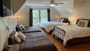 Un dormitorio con dos camas, ventilador de techo, televisor montado en la pared y ventana con cortinas.