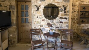 A rustic stone wall with a wooden door, two wooden chairs, a round table with a flower vase, and a wooden bench. - Chaihoutes stone villa into Olive farm in Zia (Kos)