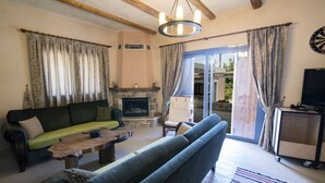 A living room with a fireplace, a sofa, a coffee table, and a television. - Chaihoutes stone villa into Olive farm in Zia (Kos)