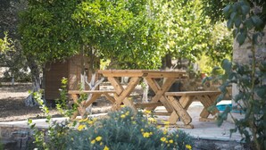 A wooden picnic table set in a garden with a stone wall and a tree providing shade. - Chaihoutes stone villa into Olive farm in Zia (Kos)