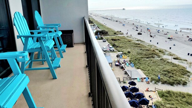 Ein Balkon mit blauen Adirondack-Stühlen, Blick auf den Strand und einen Pier in der Ferne.