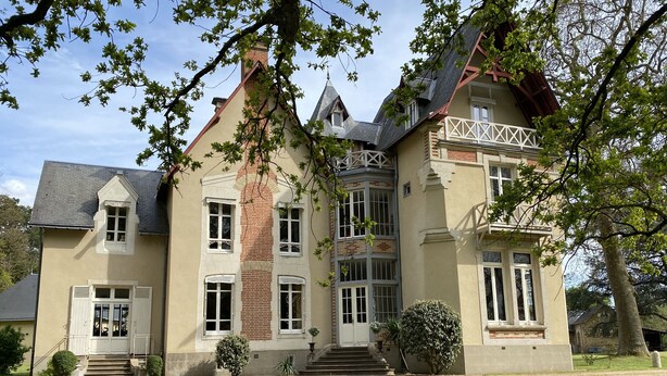 Ein großes, mehrgeschossiges Haus mit einem markanten Ziegelkamin, zahlreichen Fenstern und einem gepflegten Rasen.