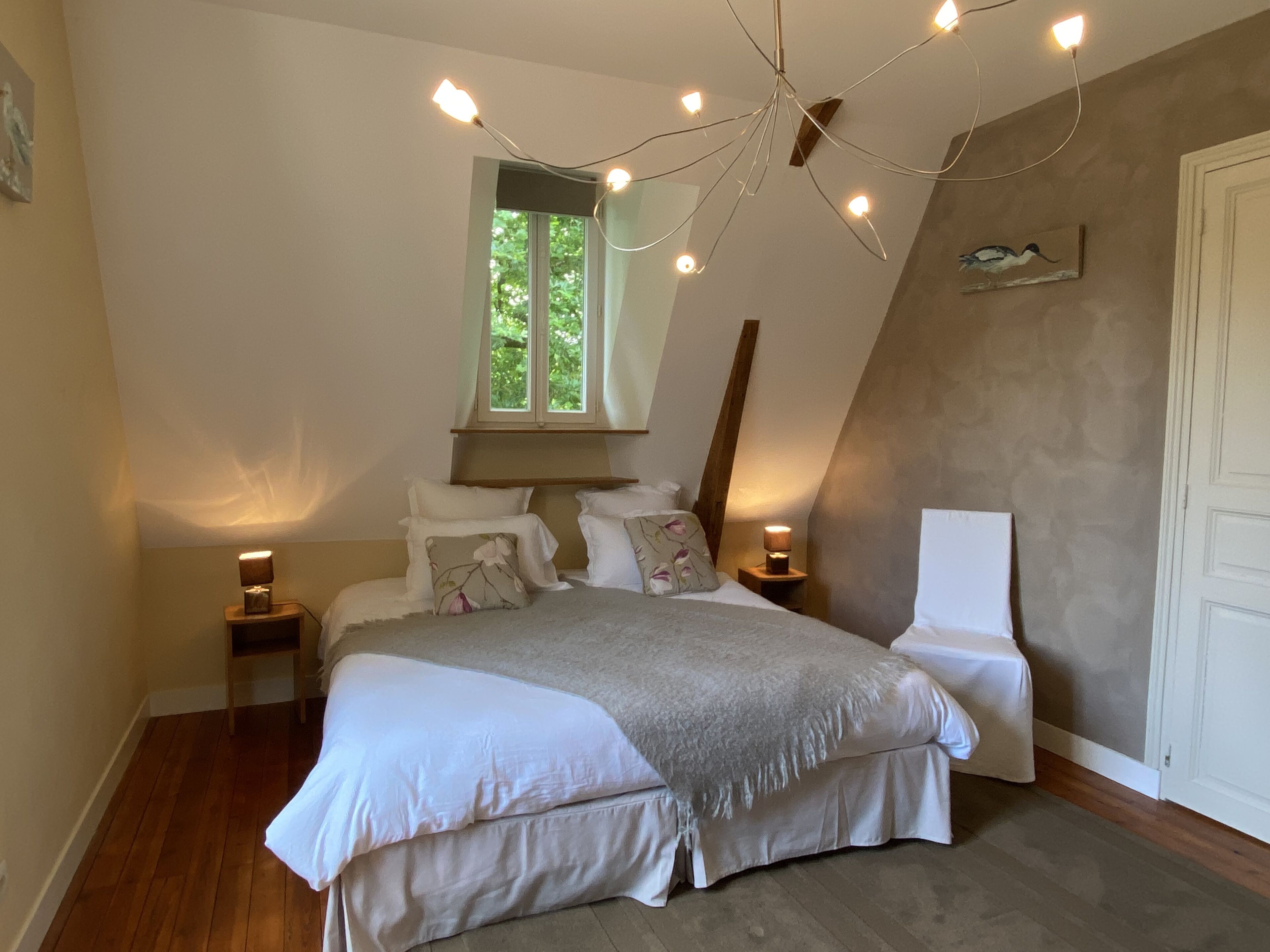 A bedroom with a large bed, a window, a chandelier, and a door.