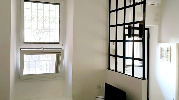 A room with a window, a TV on a stand, and a white chair. - The Baions House (Roma)