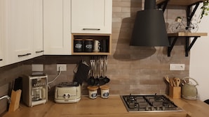 A modern kitchen with white cabinets, a built-in stove, a toaster, salt and sugar containers, and a hanging pot rack. - The Baions House (Roma)