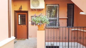 A building entrance with a wooden door, an air conditioning unit, a potted plant, and a metal railing. - The Baions House (Roma)