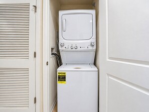 A compact, white, front-loading washing machine in a small laundry room with a door and a vent.