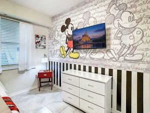 A room with a Mickey Mouse mural, a television, a red chair, and a white dresser.