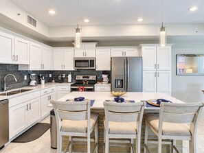 A modern kitchen with white cabinets, stainless steel appliances, and pendant lighting.