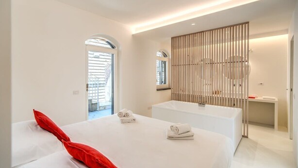 A modern hotel room with a large bed, a bathtub, and a window with blinds. - Casa Filippo by Feeling Italy (Sant'Agata sui Due Golfi)