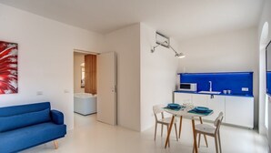 A modern living room with a blue sofa, a dining area with a white table and chairs, and a kitchen with blue cabinets and a microwave. - Casa Filippo by Feeling Italy (Sant'Agata sui Due Golfi)