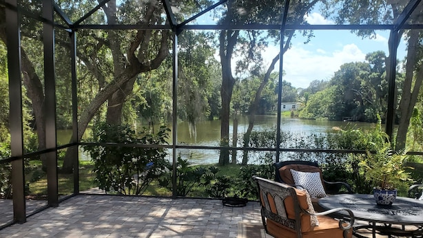 Un porche cubierto con vista a un lago, amoblado con una mesa y sillas.