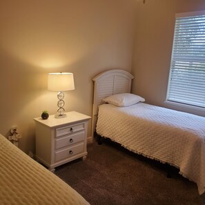 A bedroom with a single bed, a nightstand with a lamp, and a window with blinds. - Centrally located waterfront home (Merritt Island)