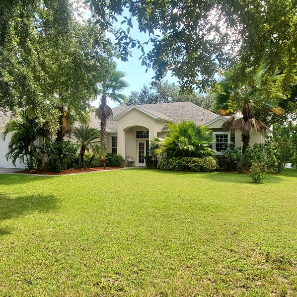 A house with a well-maintained lawn and various trees. - Centrally located waterfront home (Merritt Island)