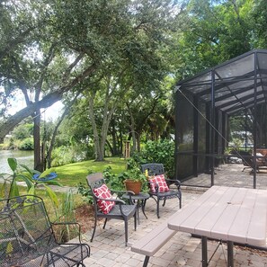 An outdoor patio with a table and chairs, surrounded by greenery and a view of a body of water. - Centrally located waterfront home (Merritt Island)
