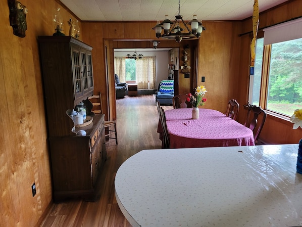A dining area with a round table covered in a pink tablecloth, a chandelier above, and wooden walls.