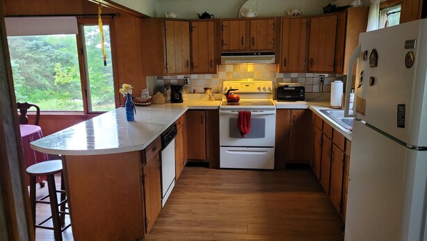 Una cocina con armarios de madera, un refrigerador blanco, una estufa y un comedor con mesa y sillas.