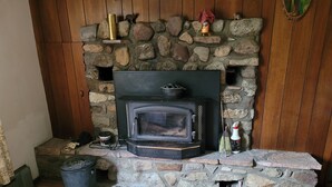 Una chimenea de piedra con un estufa de leña negra, un estante pequeño con adornos, y una escoba apoyada en la pared.