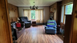 Una sala de estar con piso de madera, un sofá de cuero negro, un sillón azul y una pared de madera con un ventanal.