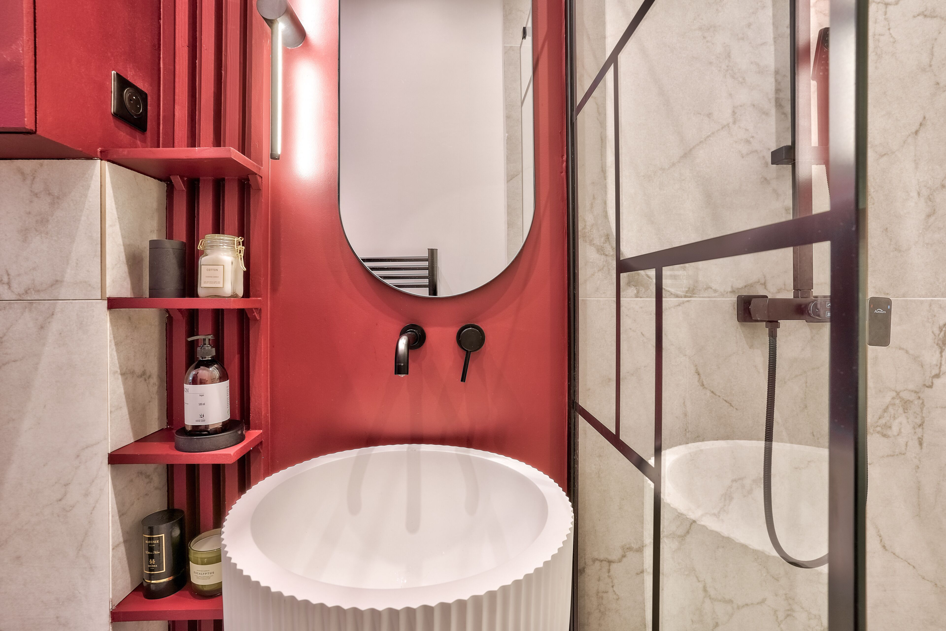 Une salle de bain avec un lavabo blanc, des étagères rouges, un miroir et un espace douche.