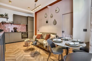 A modern kitchen with a dining area, featuring a herringbone wood floor, a sofa, and a dining table set for six. - NEW! Eiffel Tour Splendid 2BR apt in Paris (Paris)
