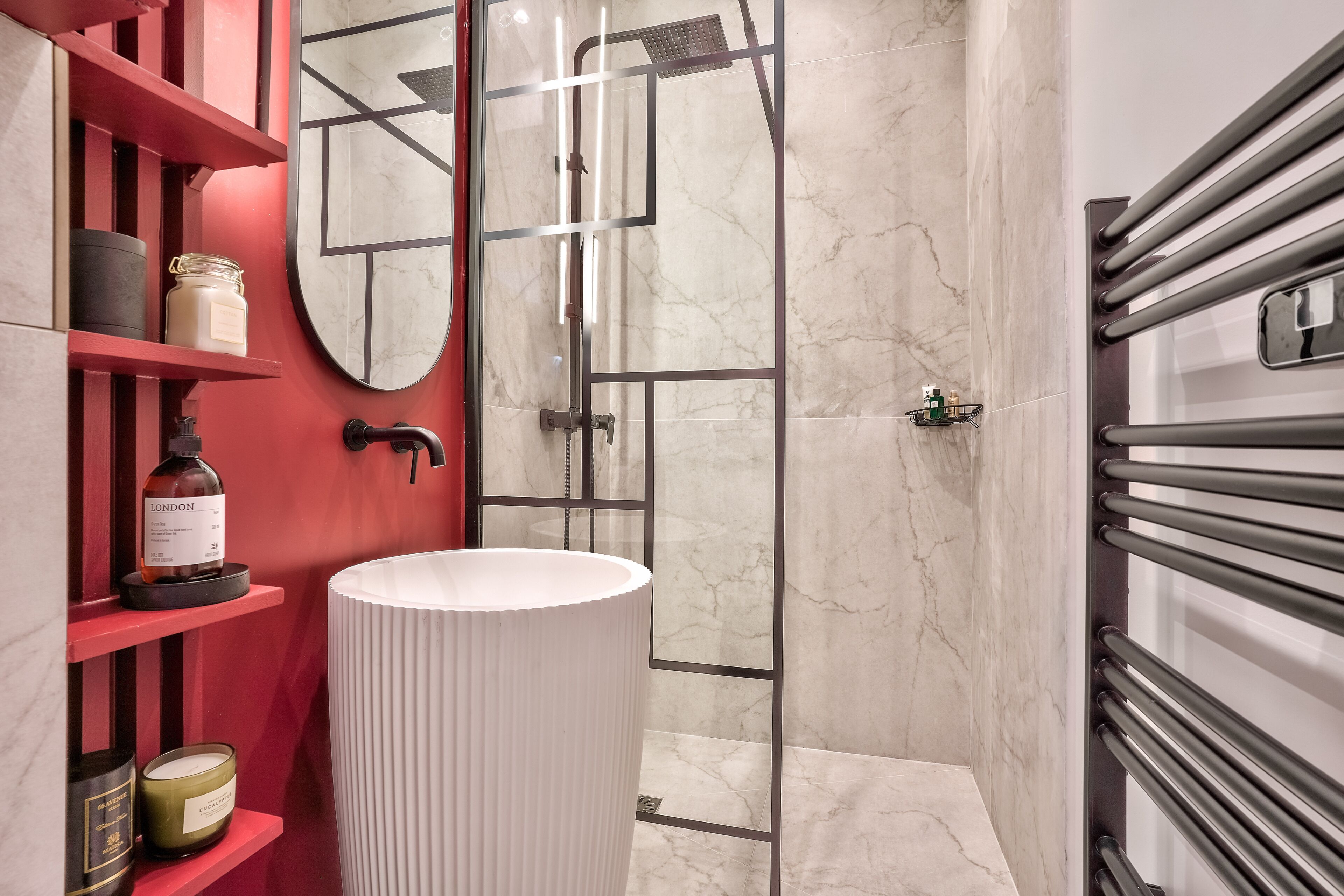 Ein modernes Badezimmer mit einem weißen Waschbecken, roten Regalen, einem Spiegel und einer Duschkabine.