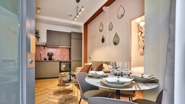 A modern dining area with a round table set for four, a kitchen in the background, and decorative wall mirrors. - NEW! Eiffel Tour Splendid 2BR apt in Paris (Paris)