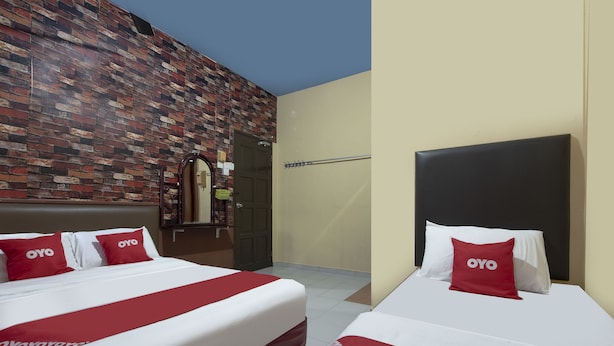 A hotel room with two beds, each with a red and white bedspread and matching pillows. The room features a brick-patterned wall and a plain beige wall. - Spot On 90305 Hen Hen Hotel (Kulai)