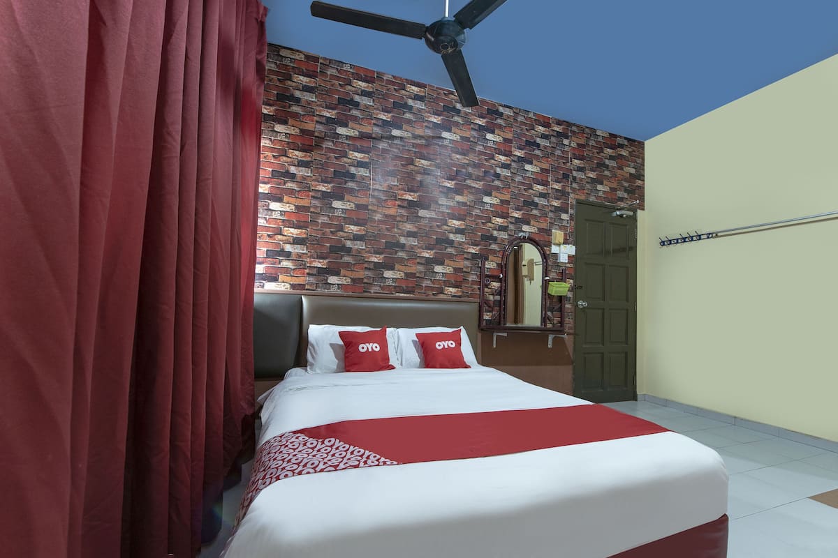 Une chambre d’hôtel avec un mur décoré d’un motif en briques, un lit avec une literie blanche et rouge, un ventilateur de plafond et une porte avec un porte-manteau.