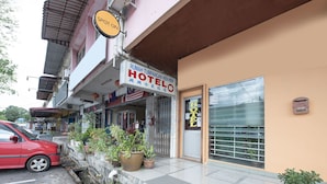A hotel entrance with a signboard, potted plants, and a parked car. - Spot On 90305 Hen Hen Hotel (Kulai)