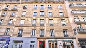Un immeuble à étages, de style architectural classique, avec un restaurant situé au rez-de-chaussée et reconnaissable à son enseigne verte.
