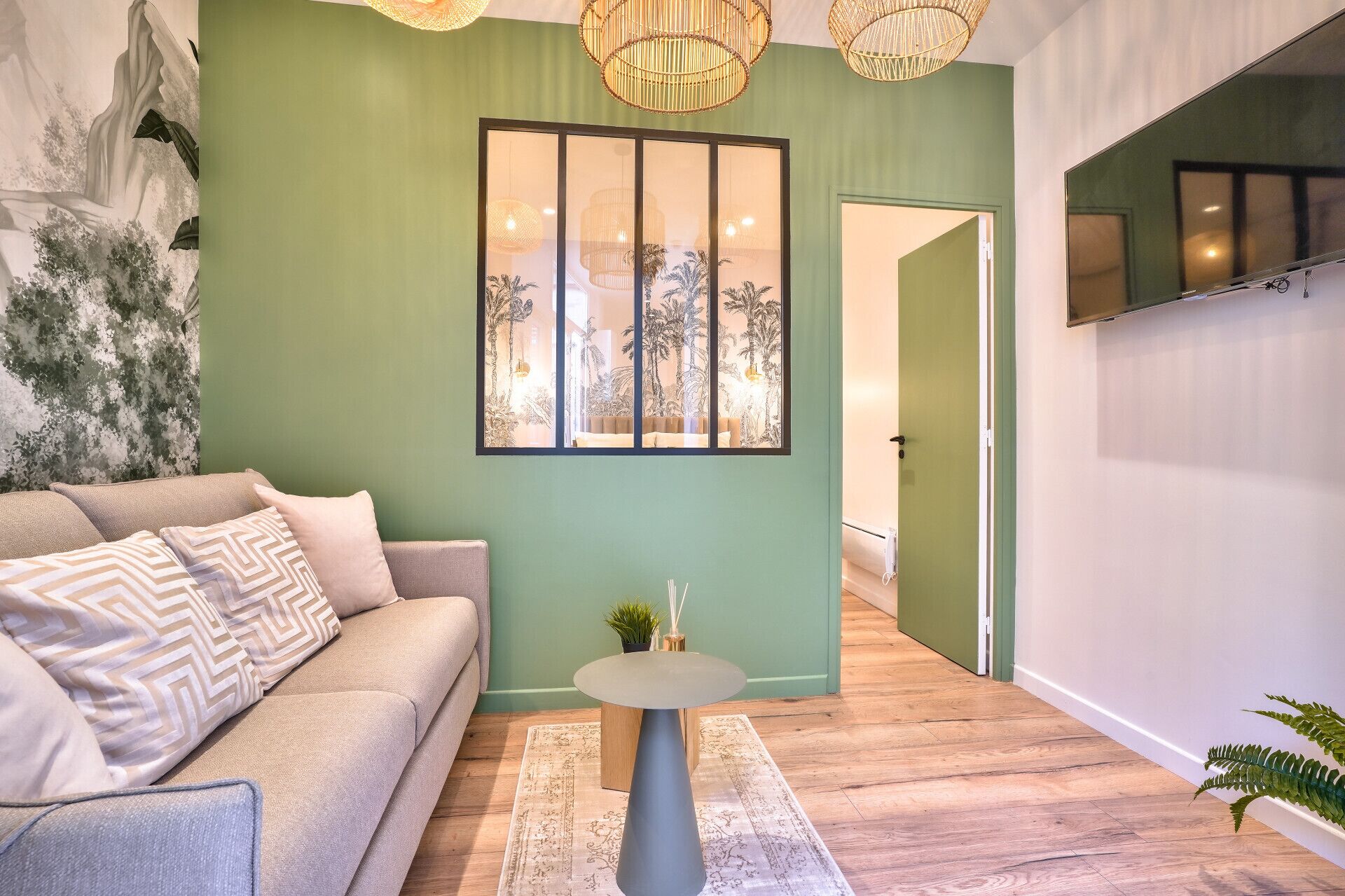 A modern living room with a green accent wall, a sofa with patterned cushions, a small round table, and a large framed artwork.