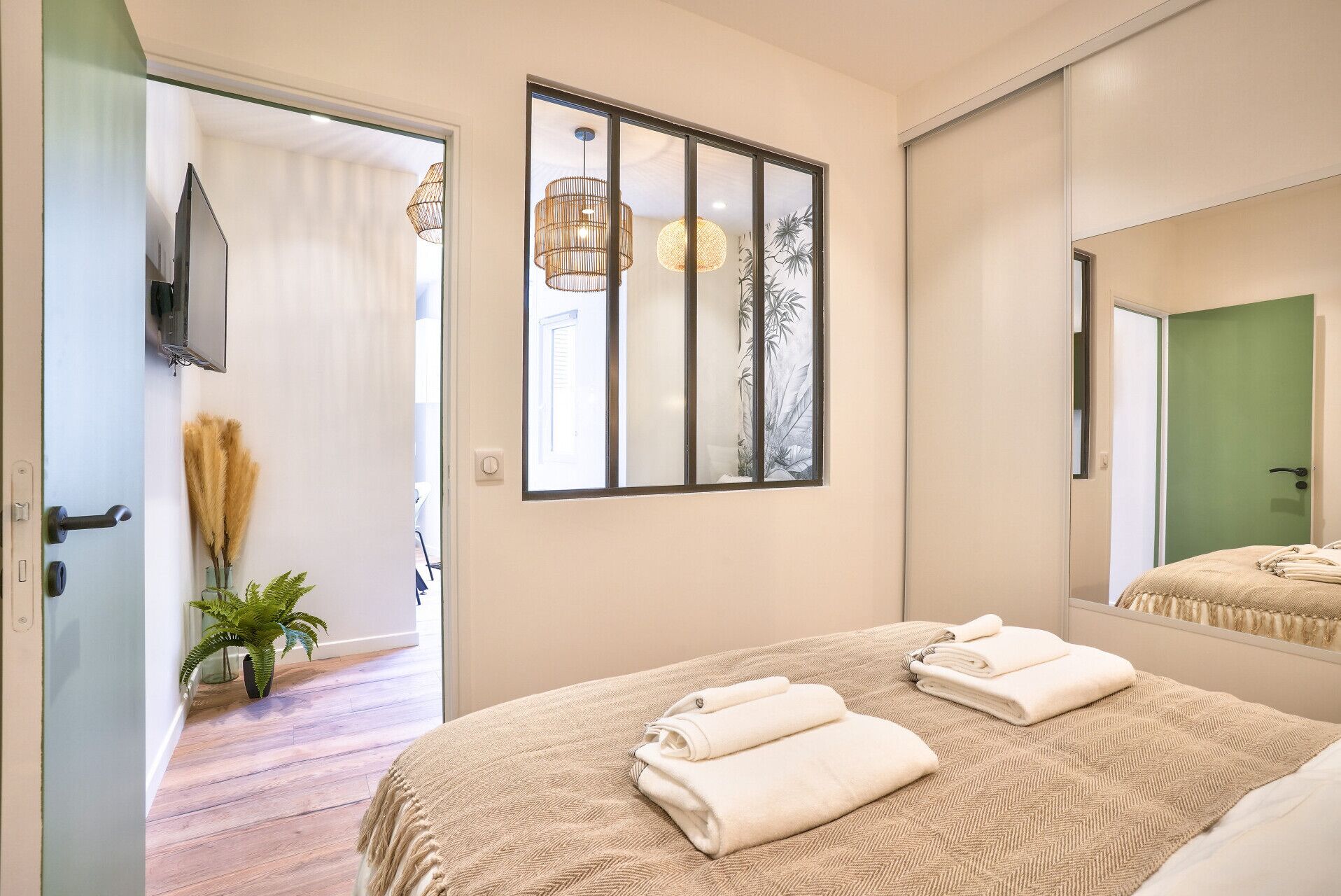 A bedroom with a bed, a large mirror, and a window with a view of a plant outside.
