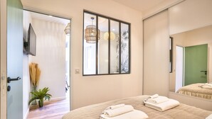 Une chambre à coucher avec un lit, un grand miroir et une fenêtre donnant sur une plante à l’extérieur.