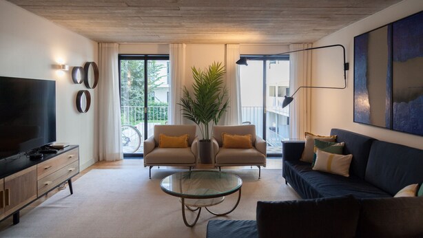 A modern living room with a TV, sofa, armchair, and a glass coffee table. - FLH Intendente Blue Flat with Balcony (Lisbon)