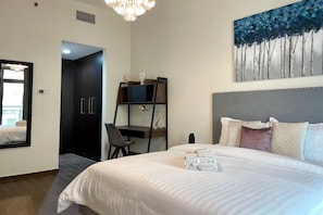 A hotel room with a bed, a desk, a chair, a painting, and a wardrobe.