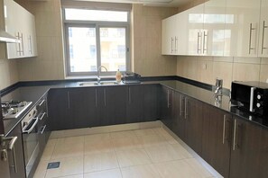 A modern kitchen with dark cabinets, a stainless steel range, and a window providing natural light. - Spacious 2BR with Direct Metro Access (Dubai)