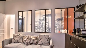 Una sala moderna con un sofá gris, tres cuadros enmarcados y una zona de cocina con un armario oscuro y una cafetera.