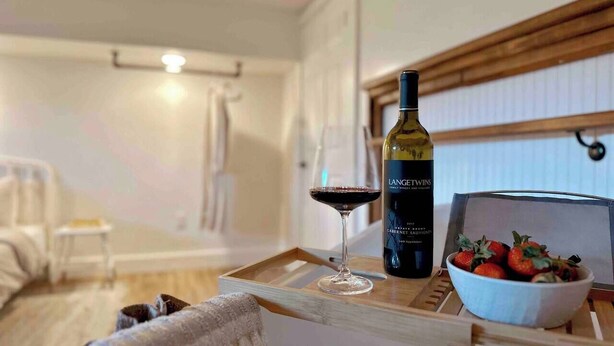 A cozy room with a wooden table holding a bottle of wine, a glass of red wine, and a bowl of strawberries. - King Apt Suite  w/ Soaker Tub & Mountain Views (Bryson City)