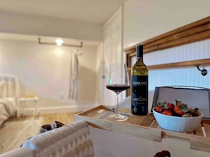 Une pièce chaleureuse où l’on trouve une table en bois sur laquelle sont posés une bouteille de vin, un verre de vin rouge et un bol de fraises.