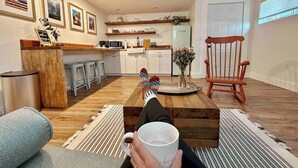A cozy living room with a coffee table, a chair, and a person holding a mug. - King Apt Suite  w/ Soaker Tub & Mountain Views (Bryson City)