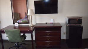 A hotel room with a desk, a chair, a television, a lamp, a dresser, and a microwave. - Royal Inn (Springdale)
