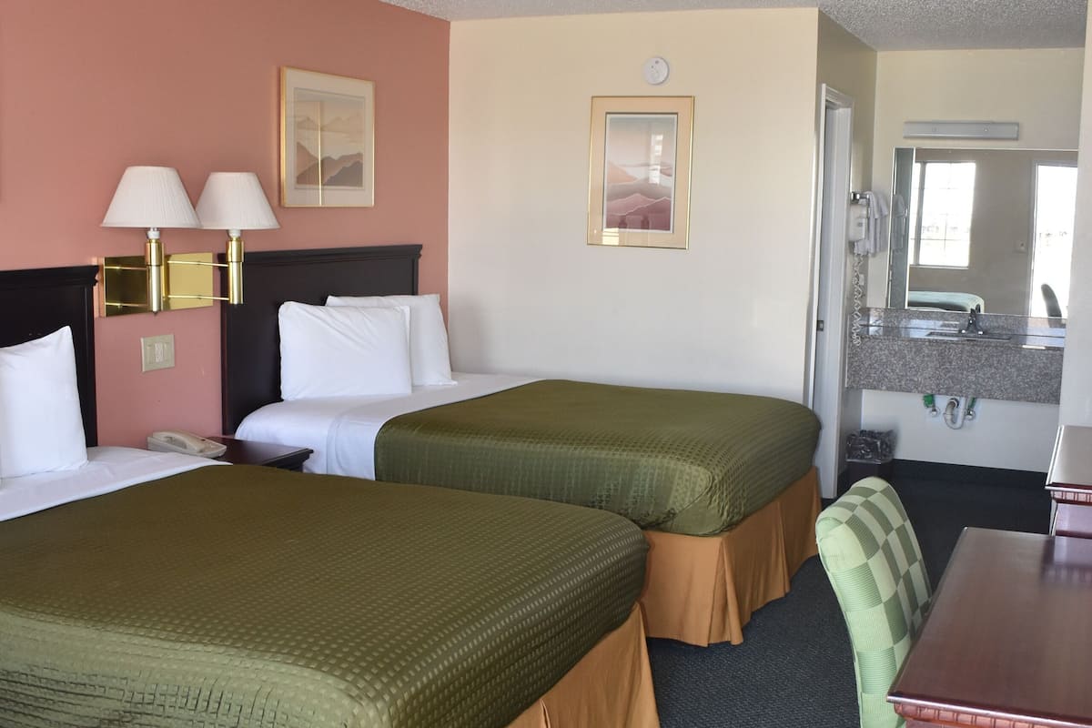 A hotel room with two beds, a desk, a chair, a mirror, and a clock on the wall.