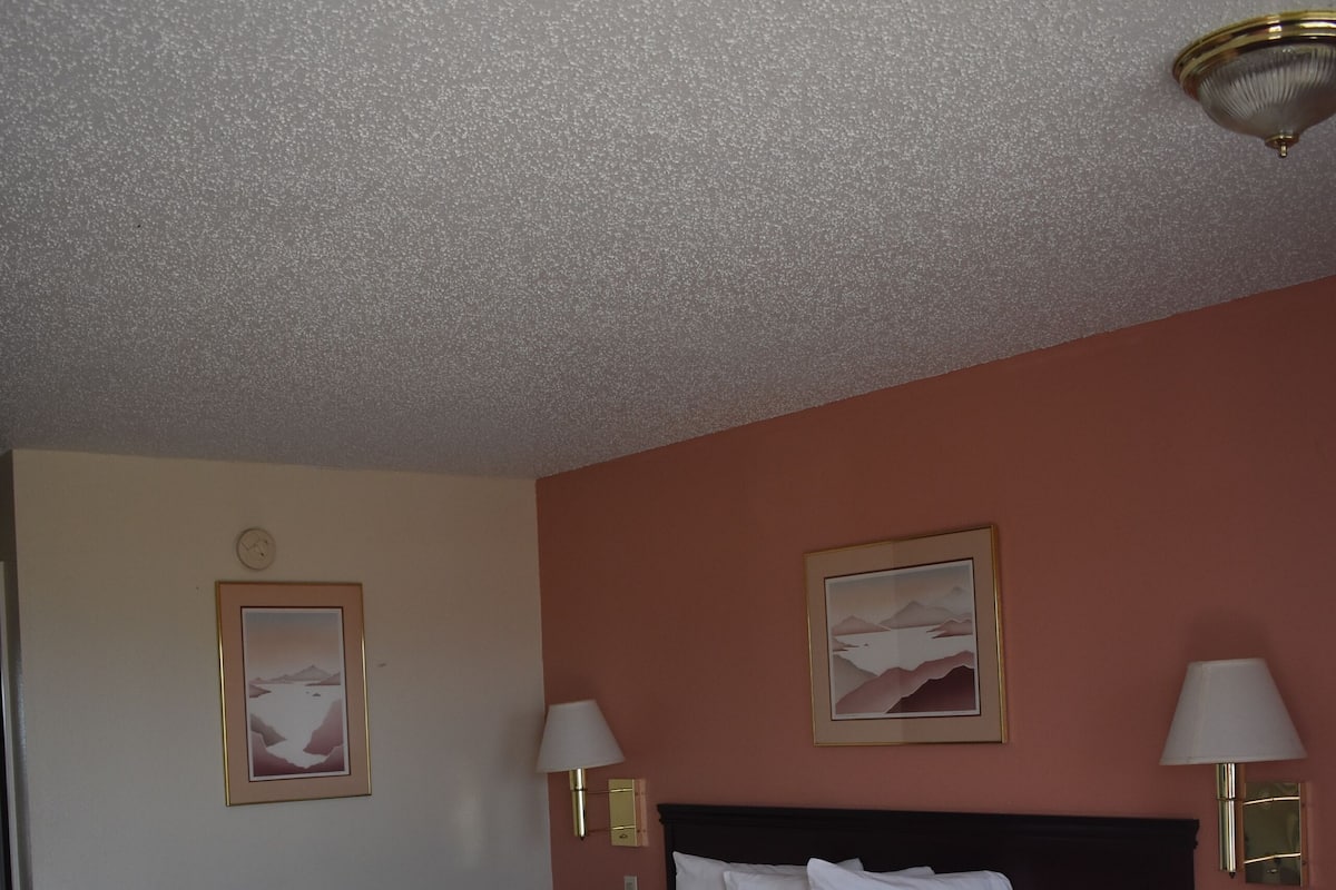 A hotel room with a large bed, two bedside lamps, a nightstand, and two framed pictures on the wall.